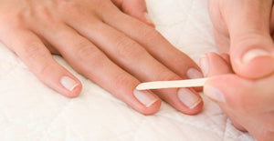 Gently pushing back cuticle with an orangewood stick after applying CND Cuticle Eraser