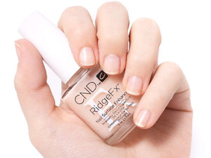 A hand with healthy nails holding a bottle of CND Ridge Fx